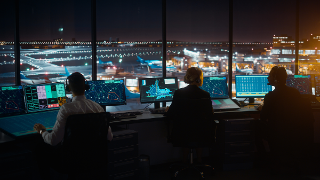 Diverse Air Traffic Control Team Working in Modern Airport Tower at Night. Office Room Full of Desktop Computer Displays with Navigation Screens, Airplane Departure and Arrival Data for Controllers.