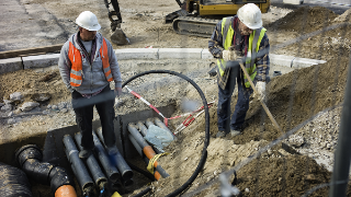 Baustelle in der zwei Bauarbeiter Wasserrohre und Leitungen unter einem Bürgersteig in Berlin verlegen.